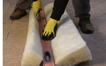 Cutting a long piece of fiberglass insulation with a level